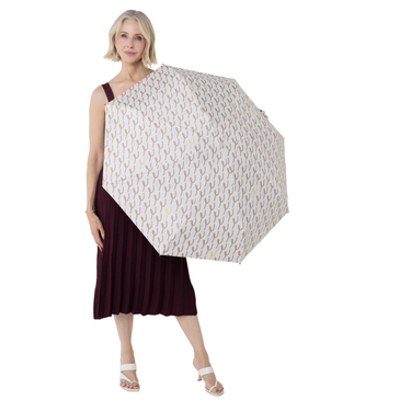 A woman holding a large open UPF50 + sun umbrella with a repeating beige and brown leaf-like pattern on a white background. She is wearing a sleeveless dark burgundy dress and white heeled sandals against a plain white studio background